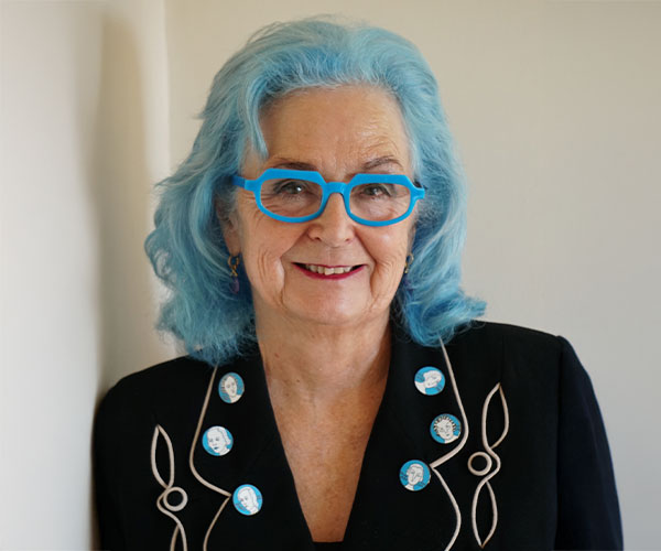 Portrait of woman with blue hair and matching blue glasses wearing black jacket